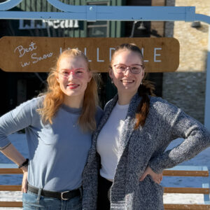 Two people stand outside wearing glasses. One is wearing rectangular glasses; the other wears pink cat-eye frames.