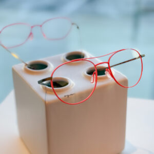 Two eyeglass frames sit atop a decorative base. One is a bright red aviator-style frame; the other is a red cat-eye.